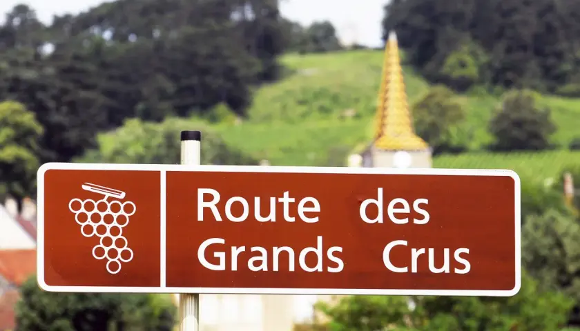 Panneau "Route des Grands Crus" en Bourgogne, promesse d'un vin rouge de Bourgogne très réputé. Paysage de vignobles et clocher doré en arrière-plan.