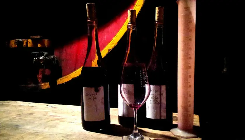Trois bouteilles de vin, un verre et une éprouvette graduée sur une table en bois, dans l'ambiance du domaine de la rectorie.