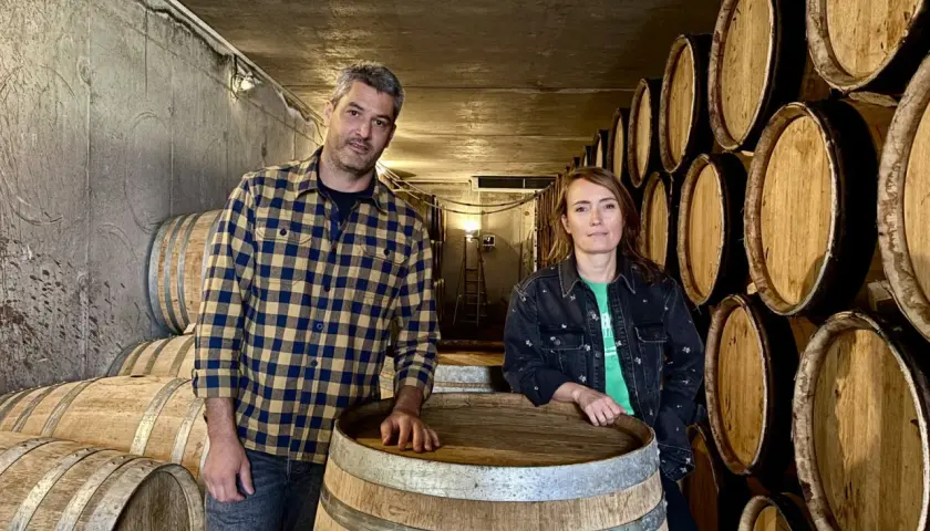 Un homme et une femme posent devant des tonneaux dans la cave du domaine Bott.