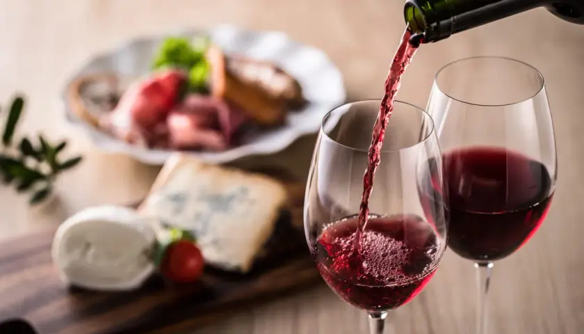Un verre de vin rouge est servi, accompagné d'un plateau de fromages et de charcuterie. Un apéritif à base de vin parfait pour partager.