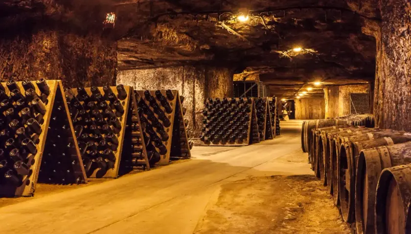 Intérieur d'une cave troglodyte, avec des rangées de bouteilles de vin sur des pupitres et des tonneaux en bois.