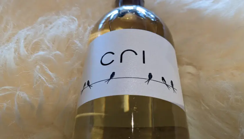 Bouteille de vin blanc "Cri" sur fond doux et texturé. Quatre petits oiseaux stylisés sont perchés sur un fil.