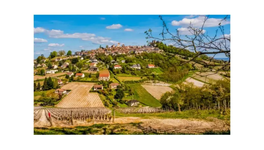 Paysage bucolique de la région de Sancerre, avec un village perché sur une colline, entouré de vignobles et de champs verdoyants sous un ciel bleu.