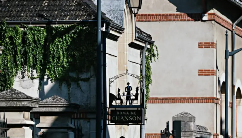 Panneau "Domaine Chanson" avec silhouettes de personnes attablées, devant un bâtiment couvert de végétation.