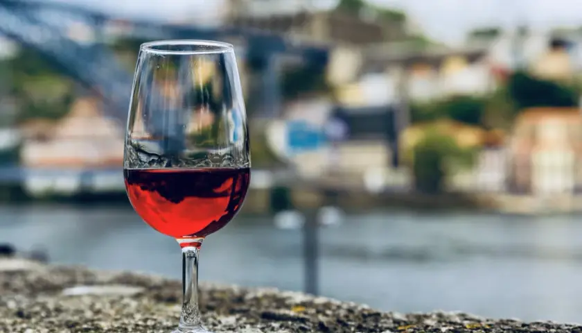 Verre de vin rouge sur un muret, avec la ville de Porto et le fleuve en arrière-plan. Une belle dégustation vin porto.