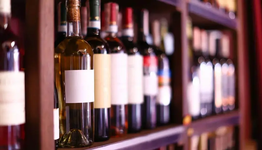 Étagères remplies de bouteilles de vin, certaines avec des étiquettes blanches vierges, prêtes à accueillir le meilleur cépage de vin rouge.