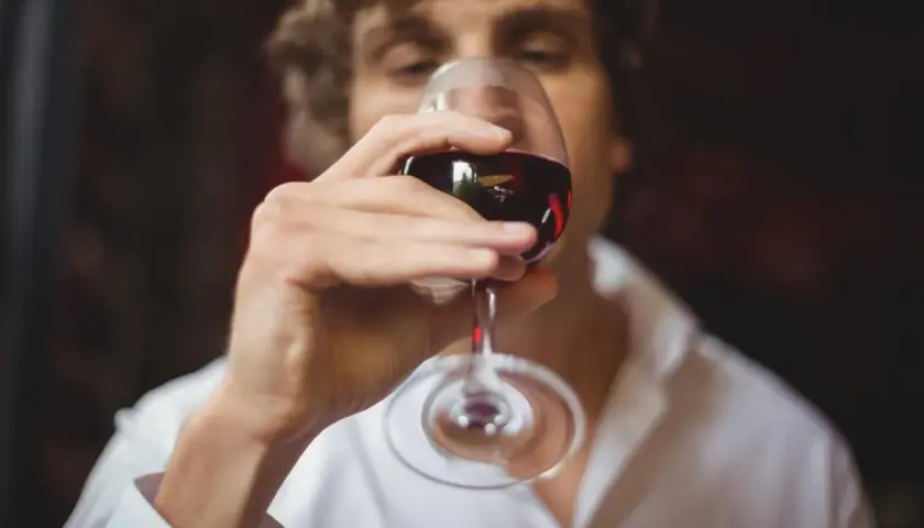 Un homme déguste un verre de vin rouge, savourant le langage du vin.