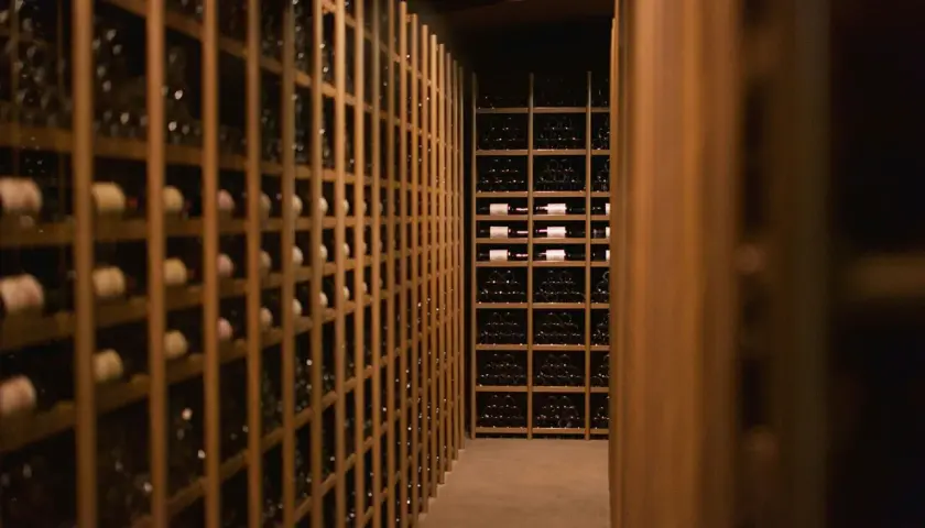Cave à vin sombre remplie de bouteilles. Des étagères en bois alignent les murs, certaines contenant des bouteilles de vin de garde 20 ans.