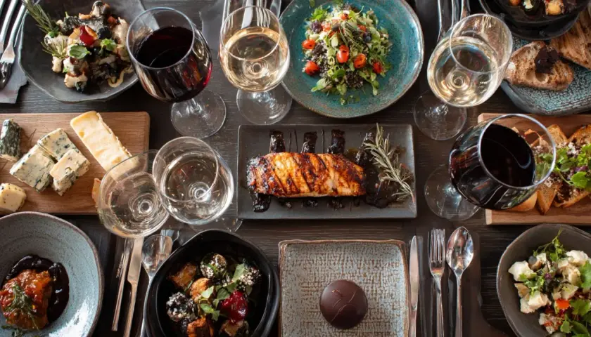 Une table dressée avec des plats variés et des verres de vin rouge et blanc. Une invitation à découvrir la fiche technique accord mets et vins.