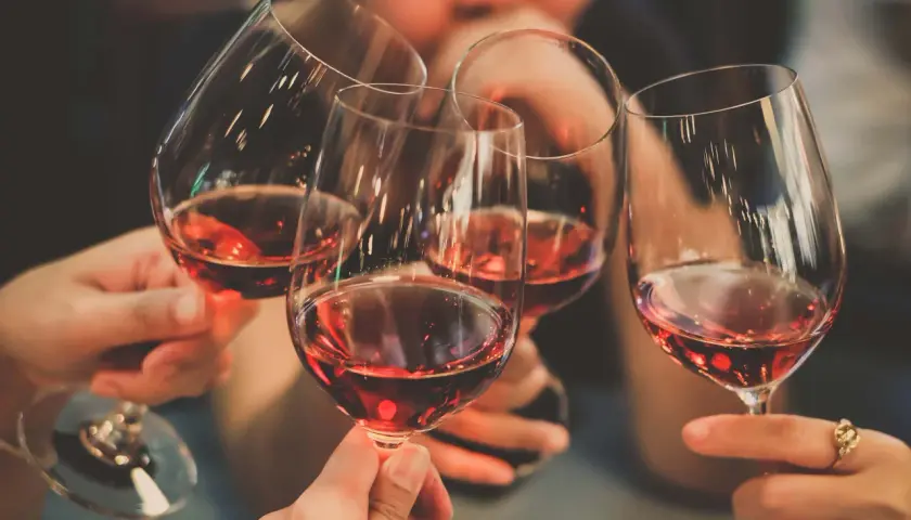 Des mains portent des verres de vin rouge pour un toast. Une invitation à tout savoir sur le vin.