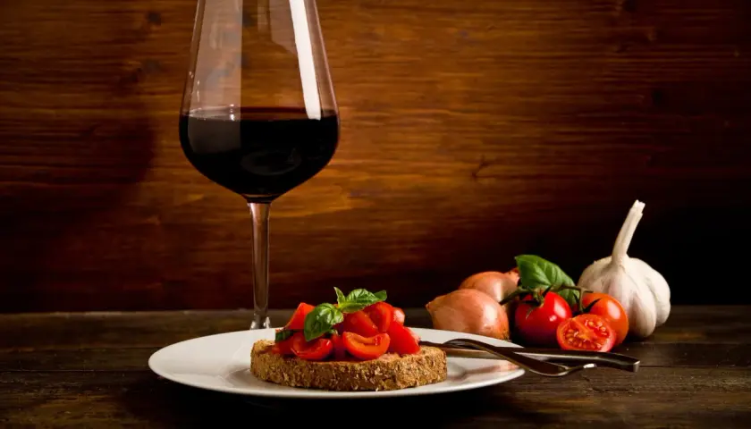Bruschetta aux tomates fraîches et basilic, accompagnée d'un verre de vin rouge passe partout. Ail et oignons en arrière-plan.
