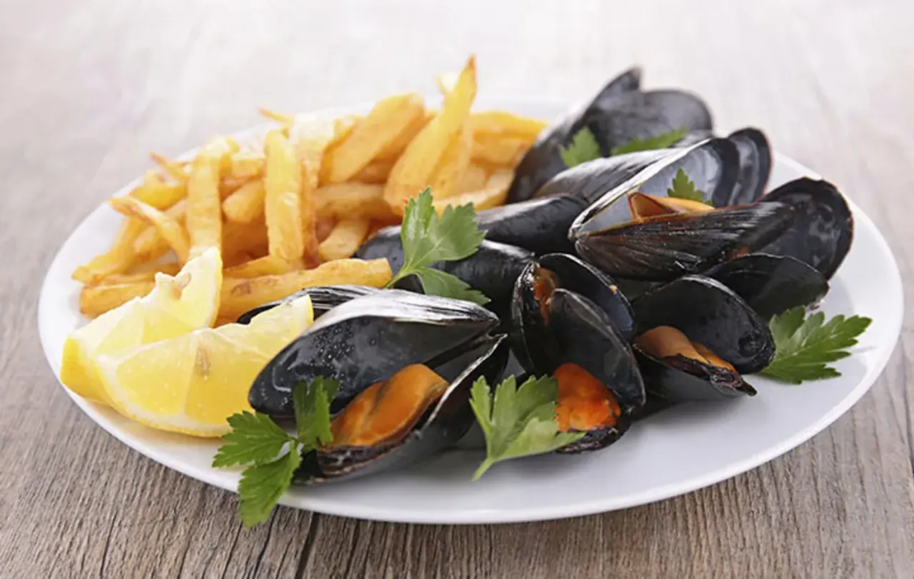 Moules frites sur une assiette blanche avec des quartiers de citron et du persil. Un plat classique, quel vin avec moules frites ?
