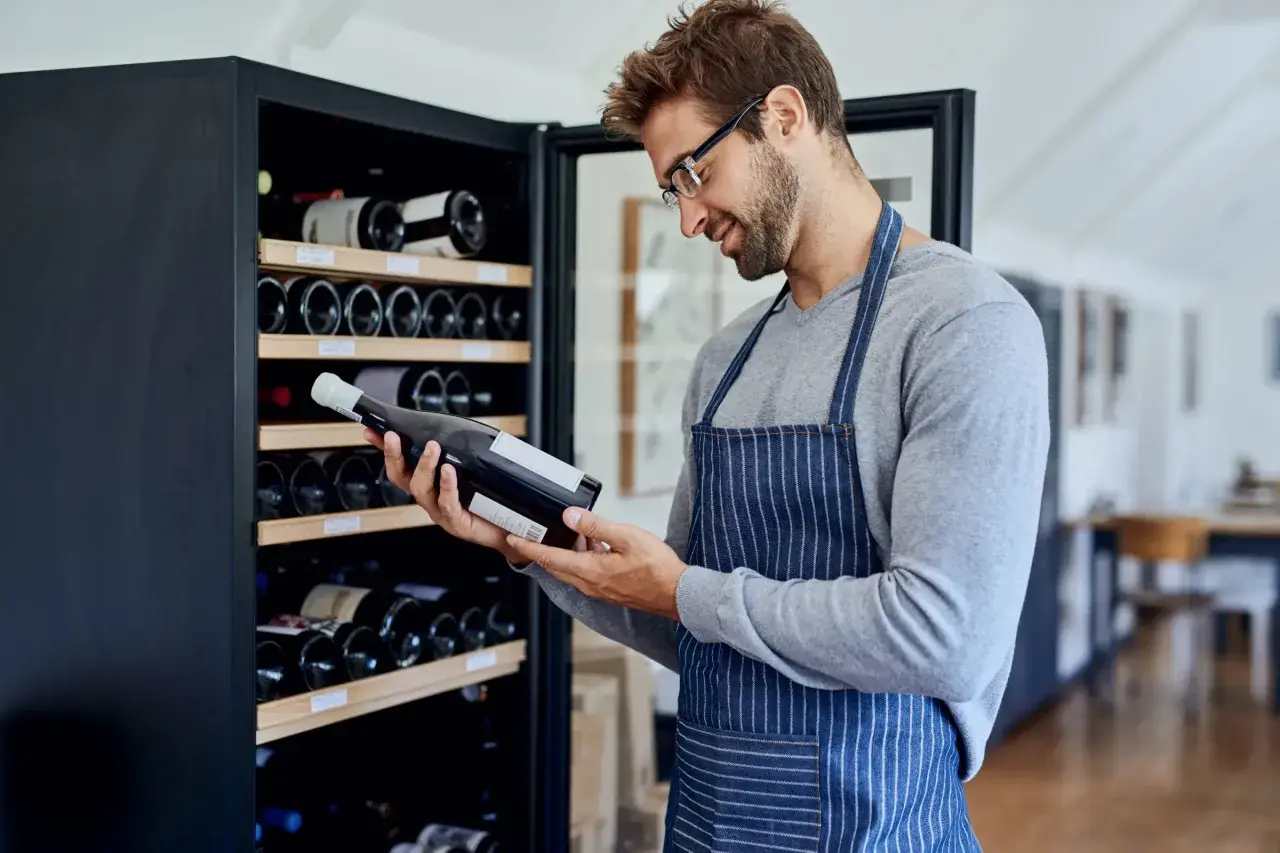 Un homme examine une bouteille de vin devant une cave à vin électrique, illustrant comment ranger une cave à vin électrique.