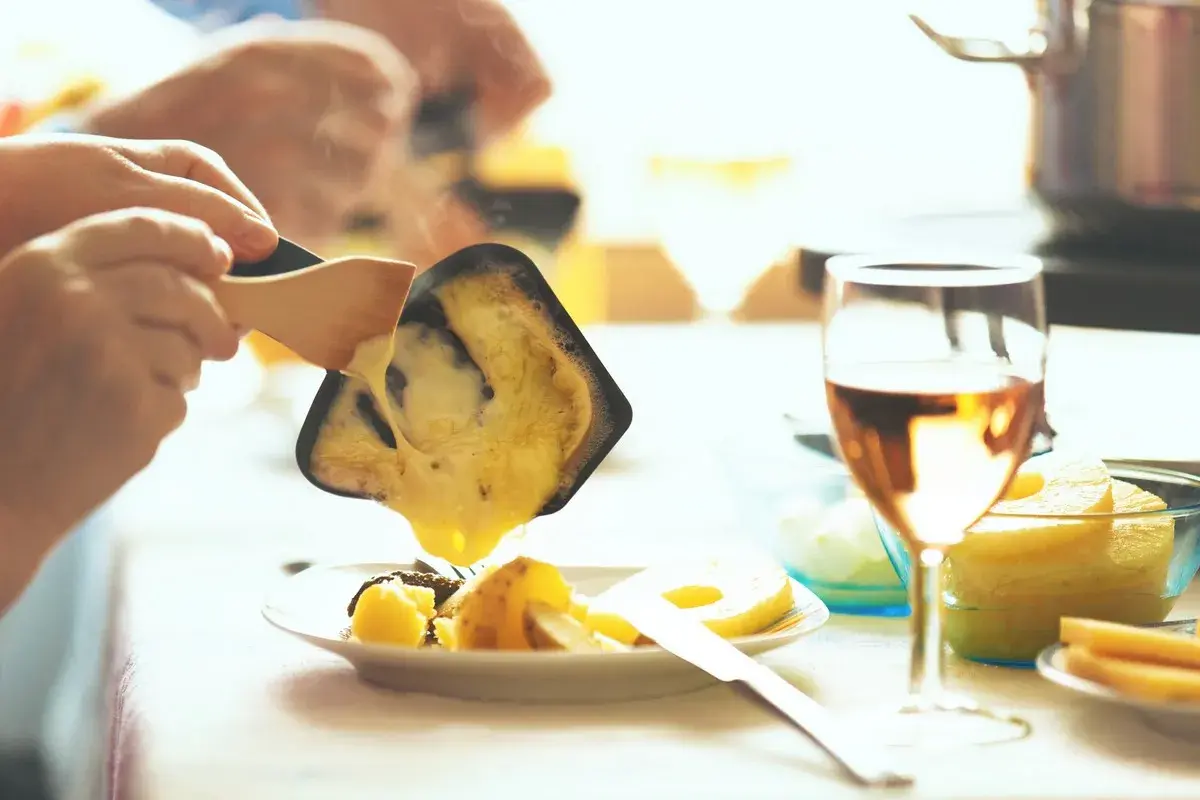 Raclette fondue dégoulinant sur des pommes de terre, un verre de vin blanc de Pouilly-Fumé à côté.