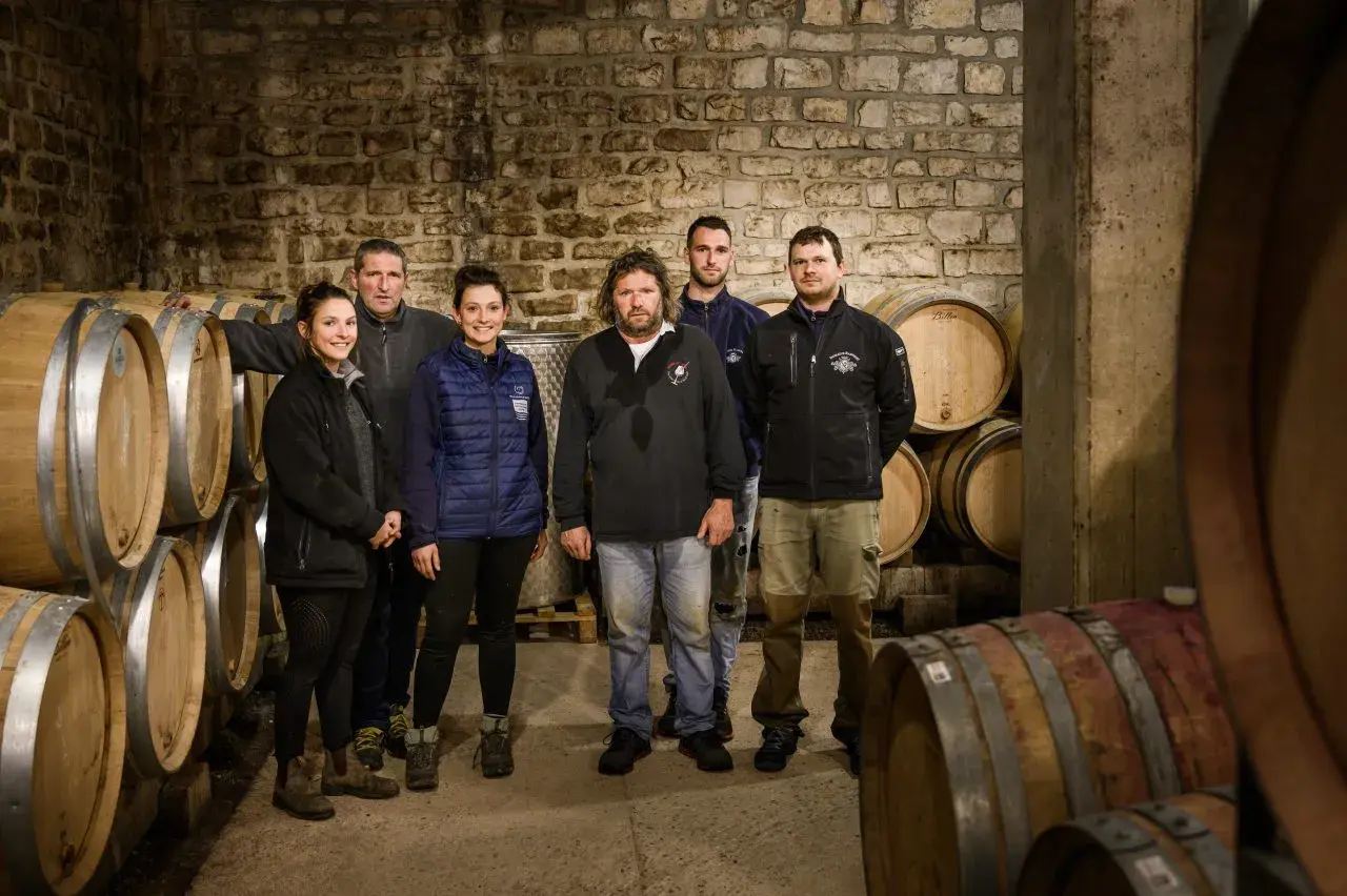 L'équipe du domaine Ramonet pose fièrement dans la cave, entourée de fûts de chêne prêts à accueillir le vin.