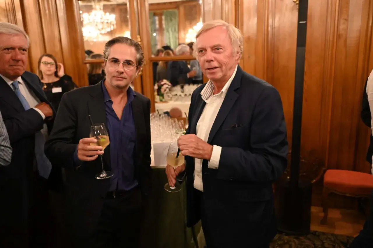 Alain Marty, à droite, avec un verre à la main, discute avec un homme à lunettes.