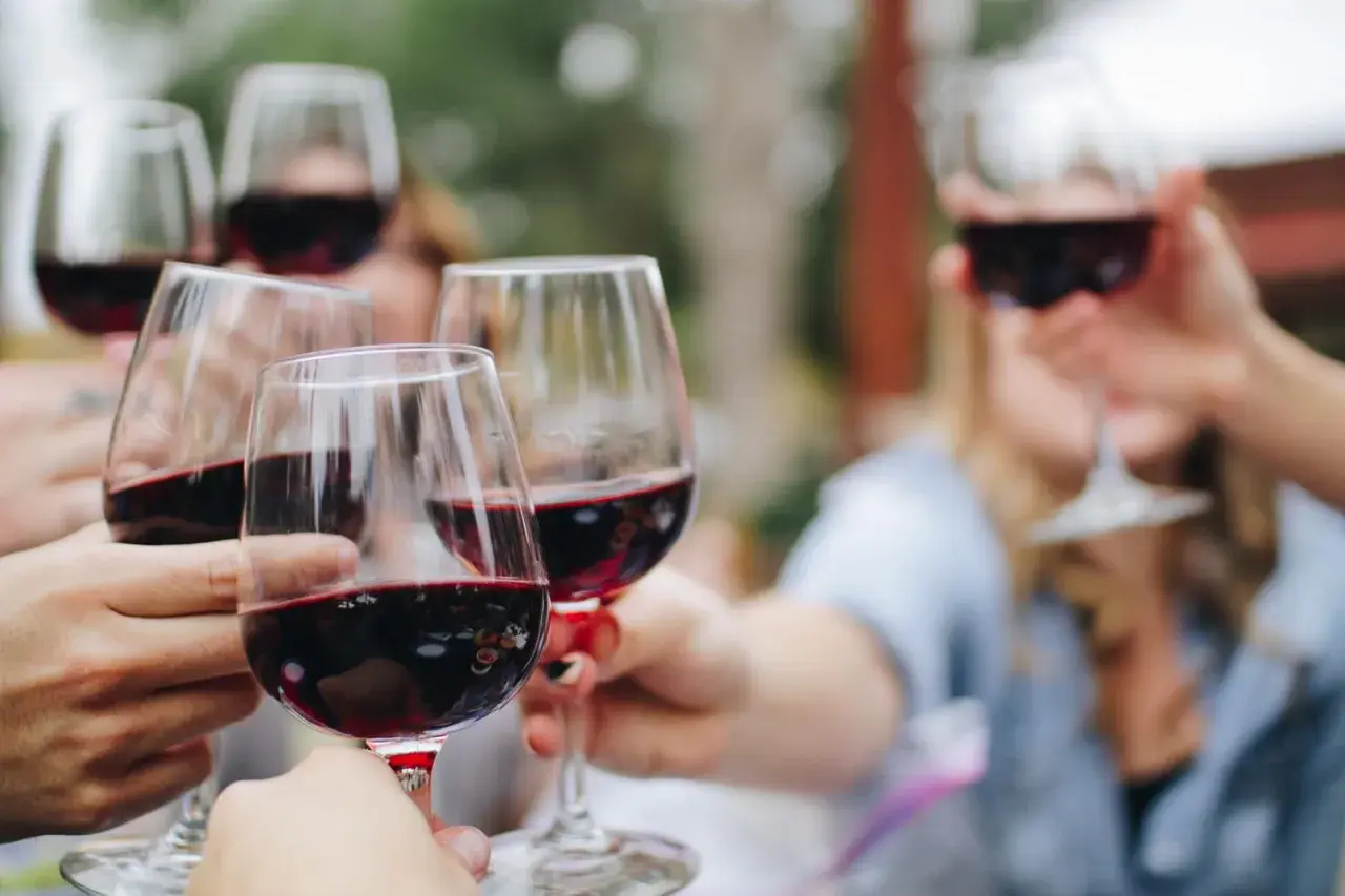 Des mains lèvent des verres de vin rouge pour un apéro convivial.