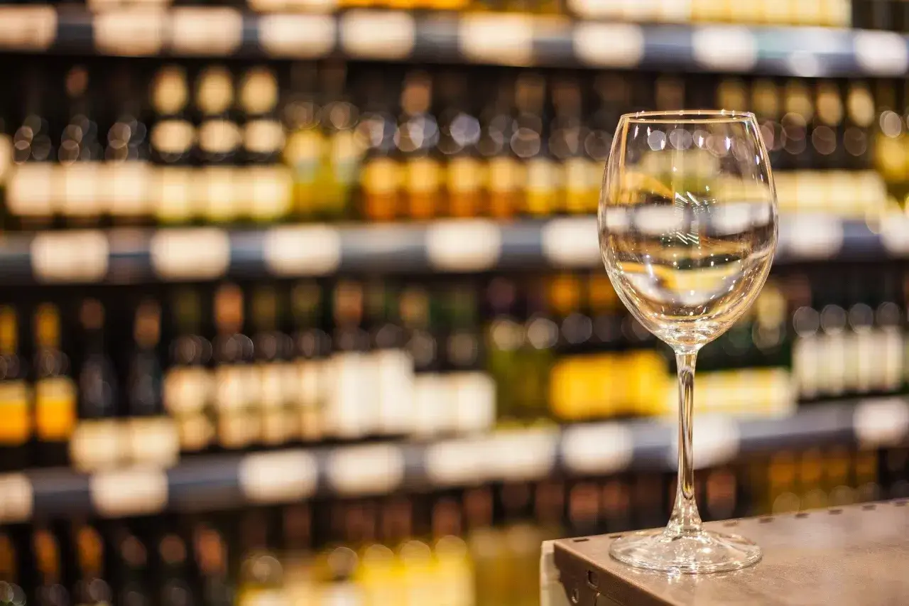 Verre à vin vide sur un comptoir, devant des étagères remplies de bouteilles. Une mise en avant foire aux vins qui invite à la dégustation.