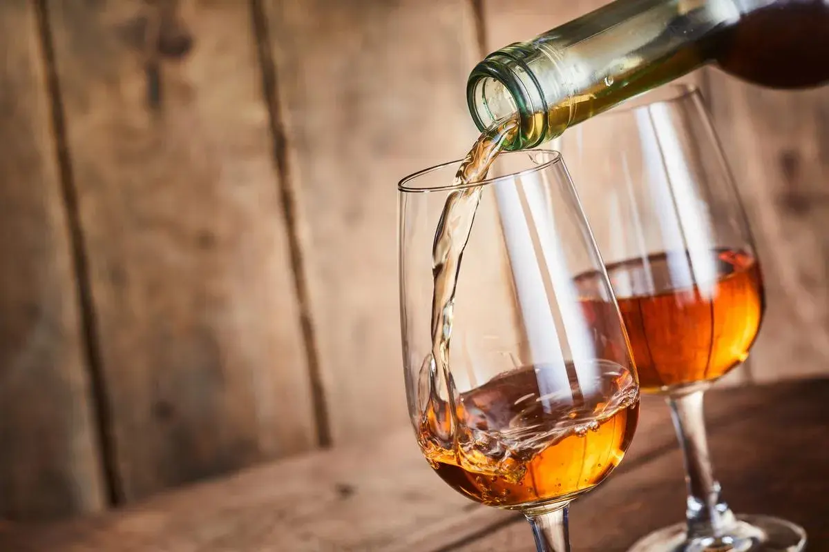 Un verre se remplit d'un vin paillé ambré, un autre verre déjà plein est à côté.