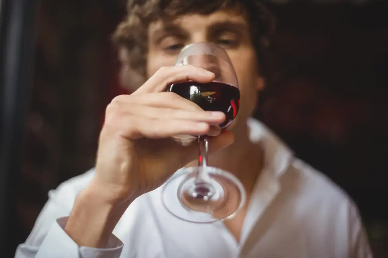 Un homme déguste un verre de vin rouge, réfléchissant aux termes pour qualifier le vin.