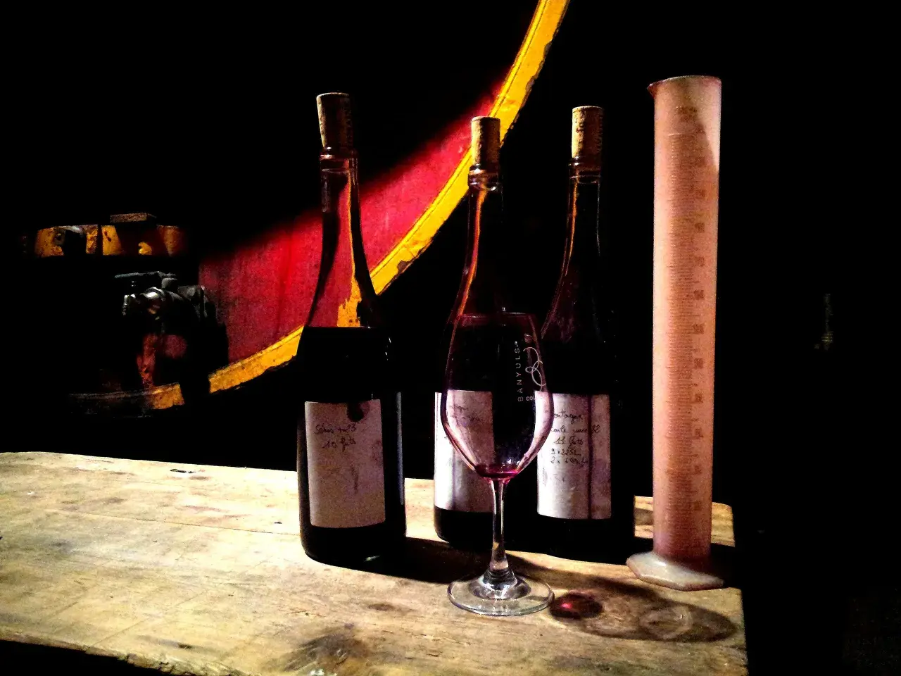 Trois bouteilles de vin, un verre et une éprouvette graduée sur une table en bois, dans l'ambiance du domaine de la rectorie.