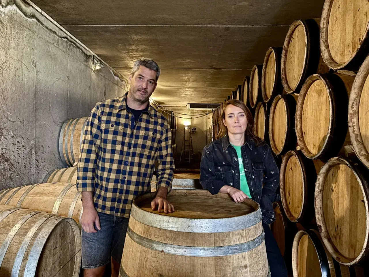 Un homme et une femme posent devant des tonneaux dans la cave du domaine Bott.