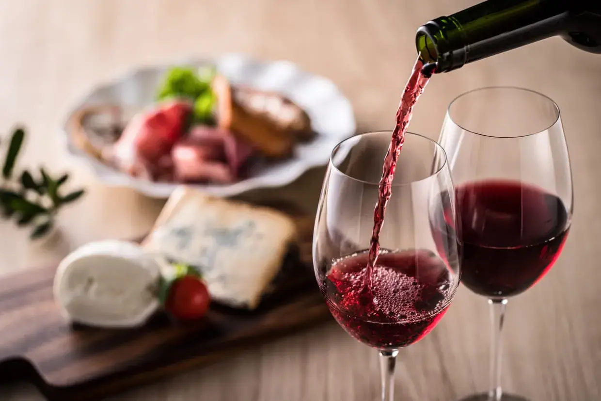 Un verre de vin rouge est servi, accompagné d'un plateau de fromages et de charcuterie. Un apéritif à base de vin parfait pour partager.