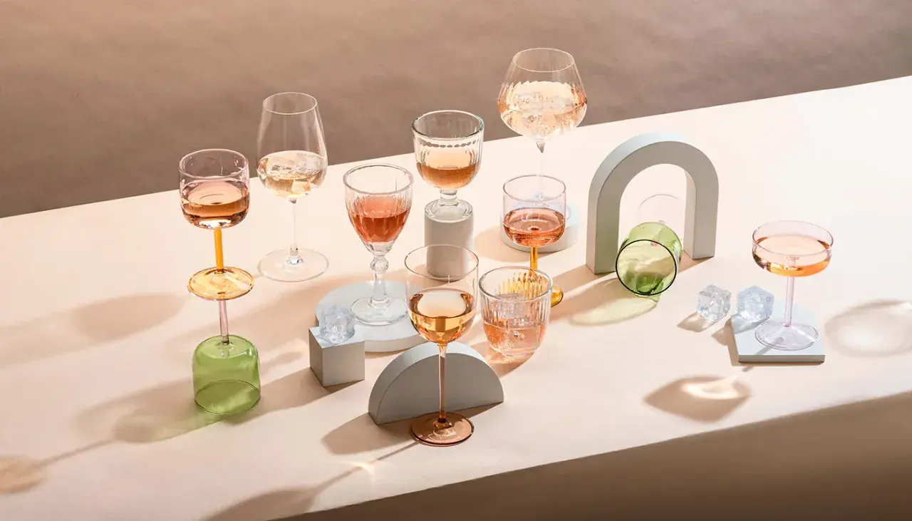 Plusieurs verres de vin blanc ou rosé, certains avec des glaçons, sont disposés sur un fond neutre.
