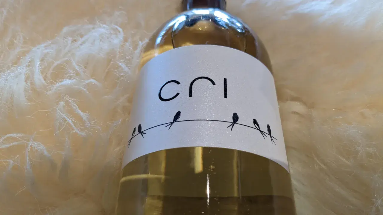 Bouteille de vin blanc "Cri" sur fond doux et texturé. Quatre petits oiseaux stylisés sont perchés sur un fil.