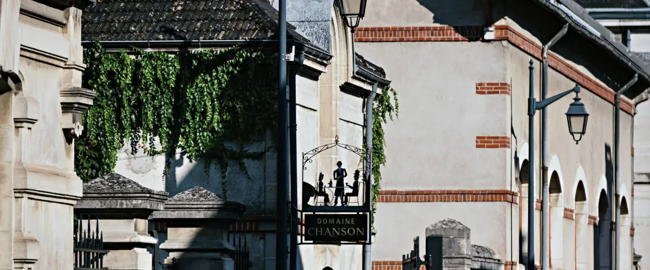 Panneau "Domaine Chanson" avec silhouettes de personnes attablées, devant un bâtiment couvert de végétation.