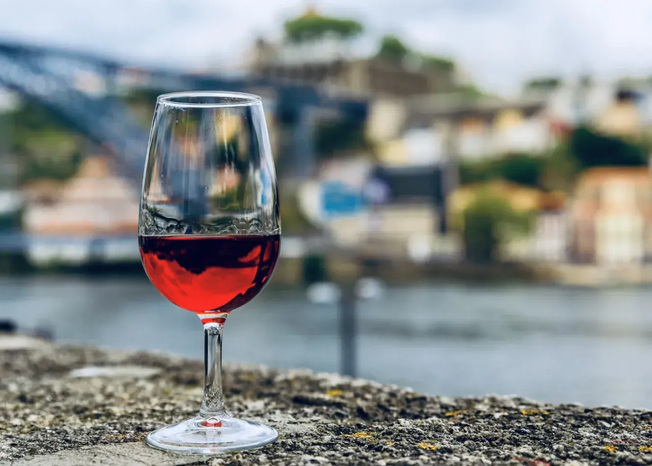 Verre de vin rouge sur un muret, avec la ville de Porto et le fleuve en arrière-plan. Une belle dégustation vin porto.