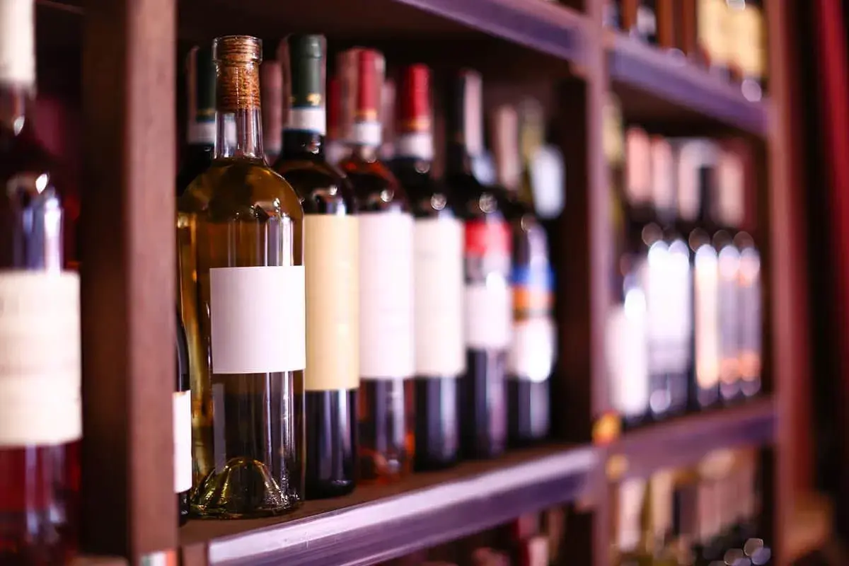 Étagères remplies de bouteilles de vin, certaines avec des étiquettes blanches vierges, prêtes à accueillir le meilleur cépage de vin rouge.