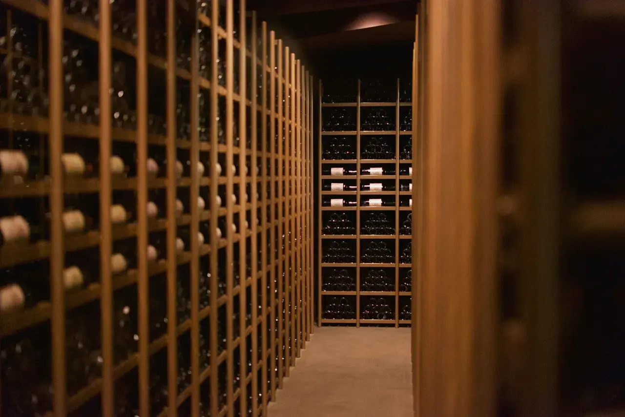 Cave à vin sombre remplie de bouteilles. Des étagères en bois alignent les murs, certaines contenant des bouteilles de vin de garde 20 ans.