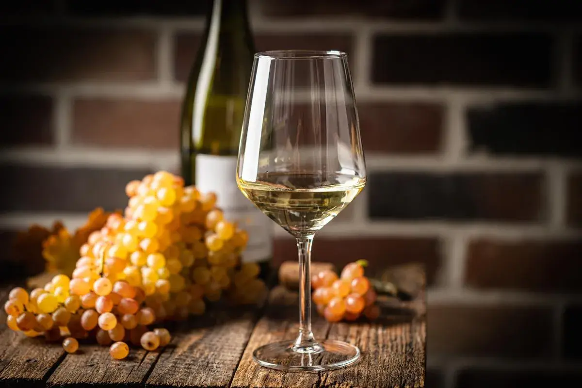 Verre de vin blanc, grappes de raisins dorés et bouteille sur fond de briques. Le chardonnay est-il un vin sec ? La réponse est dans le verre.