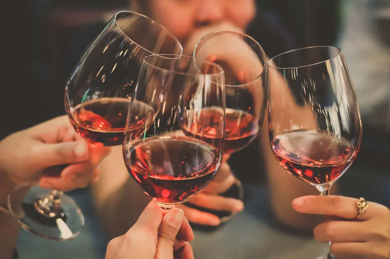 Des mains portent des verres de vin rouge pour un toast. Une invitation à tout savoir sur le vin.