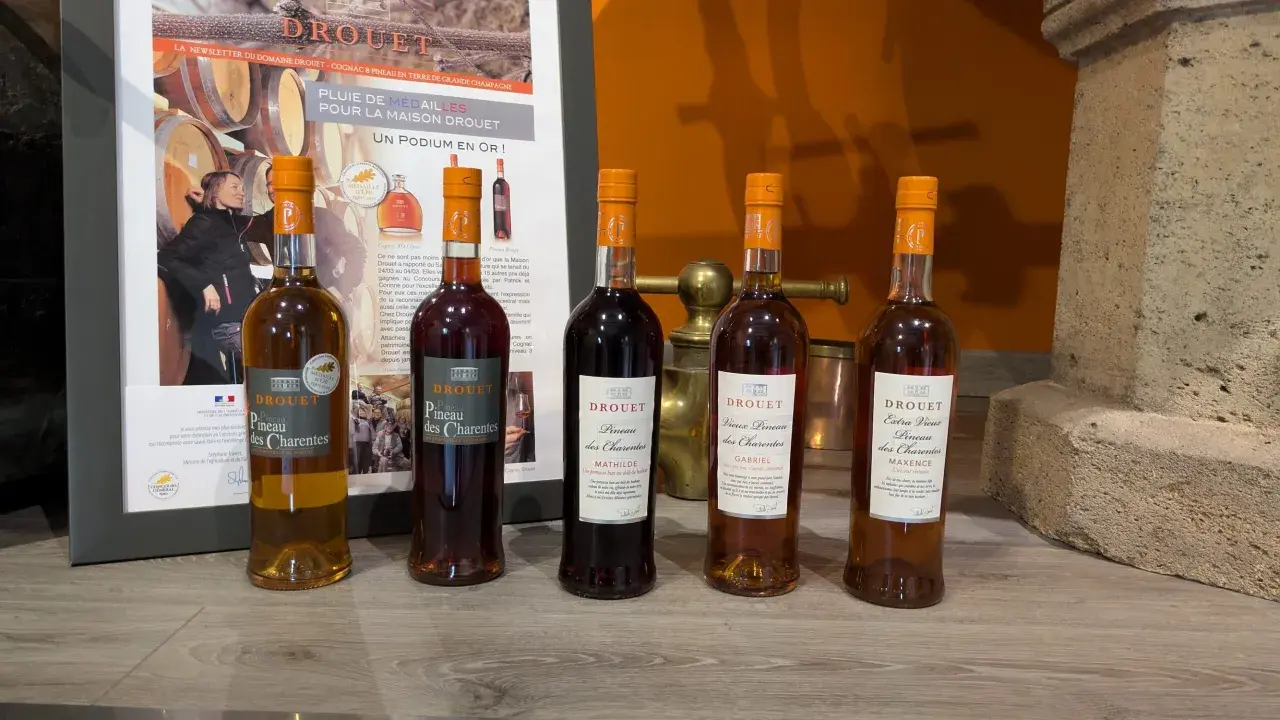 Cinq bouteilles de Pineau des Charentes Drouet, dont le meilleur pineau des Charentes, sur un fond de promotion du domaine.