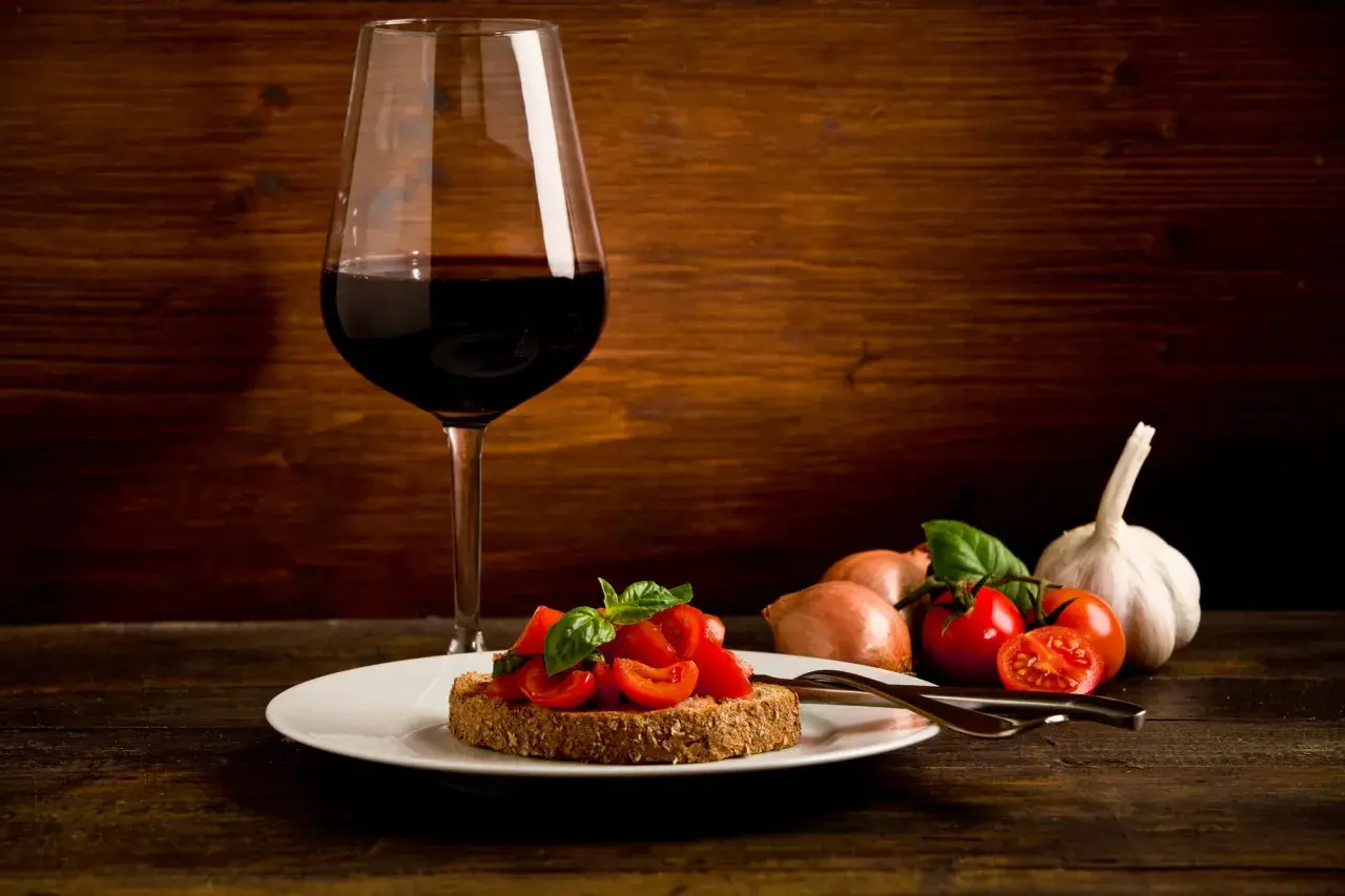 Bruschetta aux tomates fraîches et basilic, accompagnée d'un verre de vin rouge passe partout. Ail et oignons en arrière-plan.