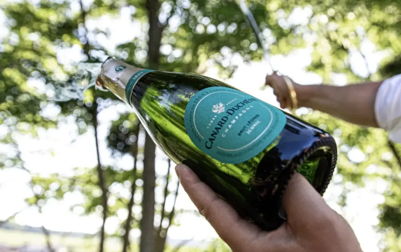 Bouteille de champagne Canard-Duchêne s'ouvrant, avec des bulles jaillissant. Un avis sur ce champagne iconique.