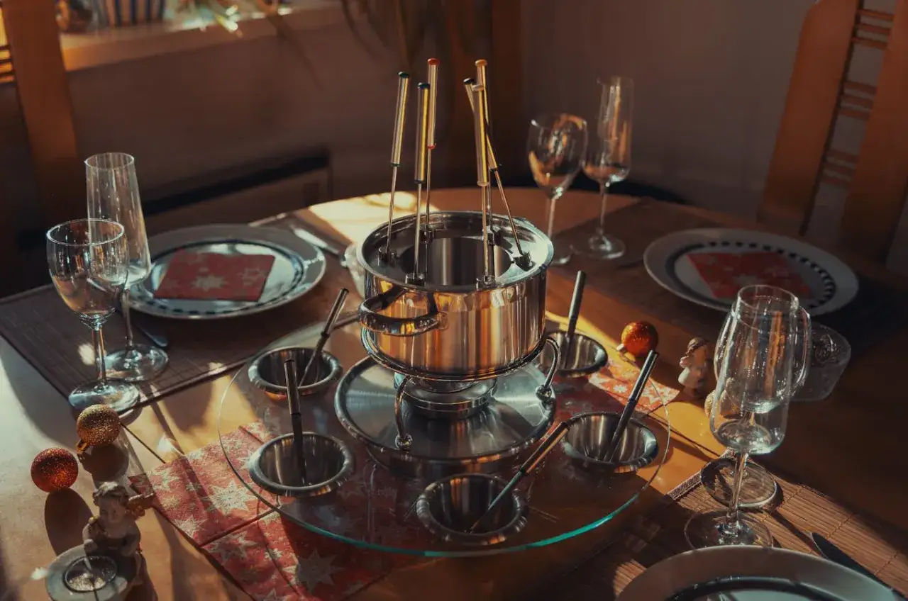 Table dressée pour une fondue chinoise, avec un appareil à fondue, des bols, des assiettes et des verres. Le vin attend patiemment.