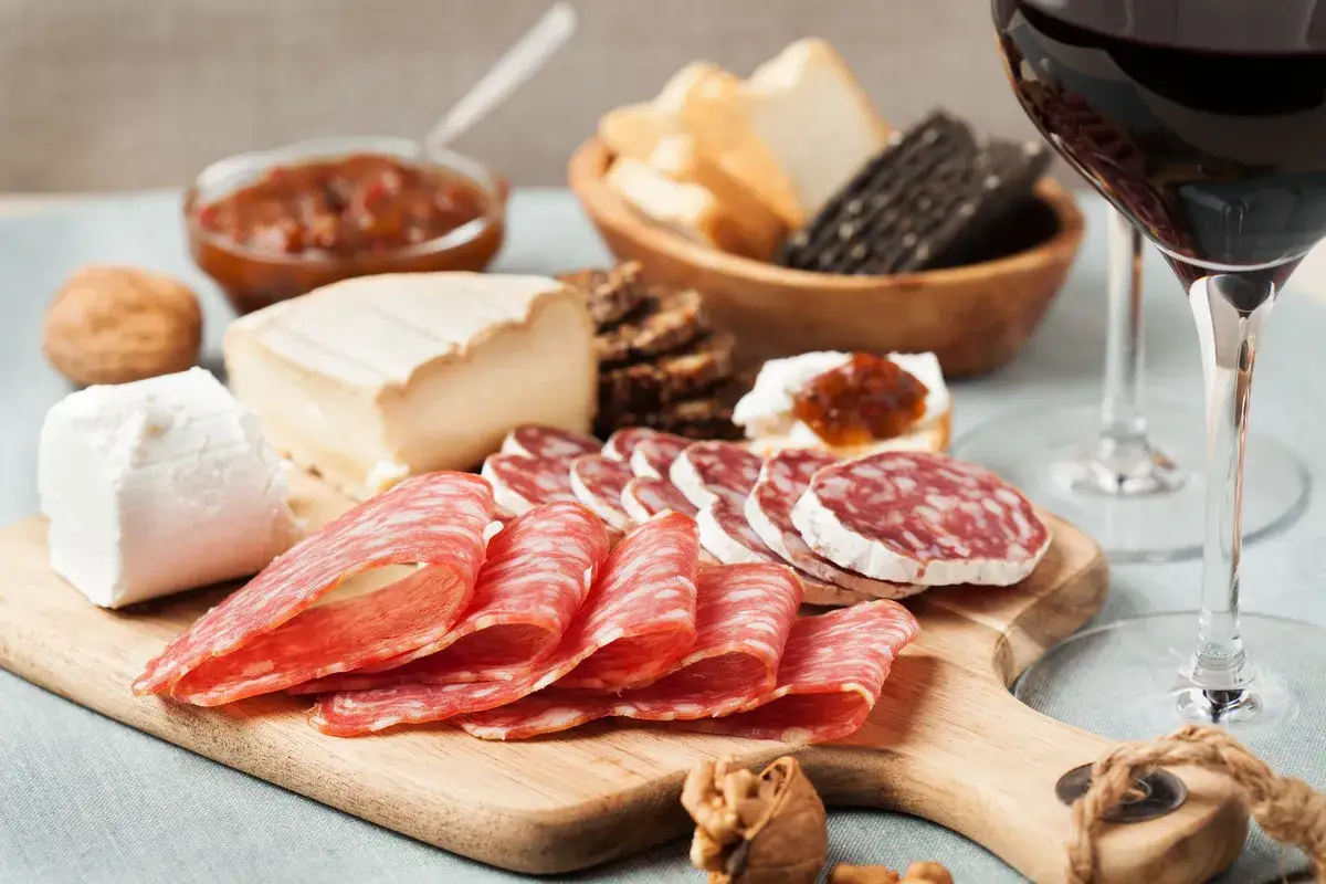 Un verre de vin rouge accompagne un plateau de charcuterie, fromages, pain et confiture. Parfait pour un ap&eacute;ro !
