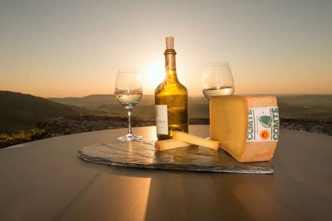 Un coucher de soleil sur le Jura, avec un verre de vin jaune du Jura, une bouteille et du fromage Comté.