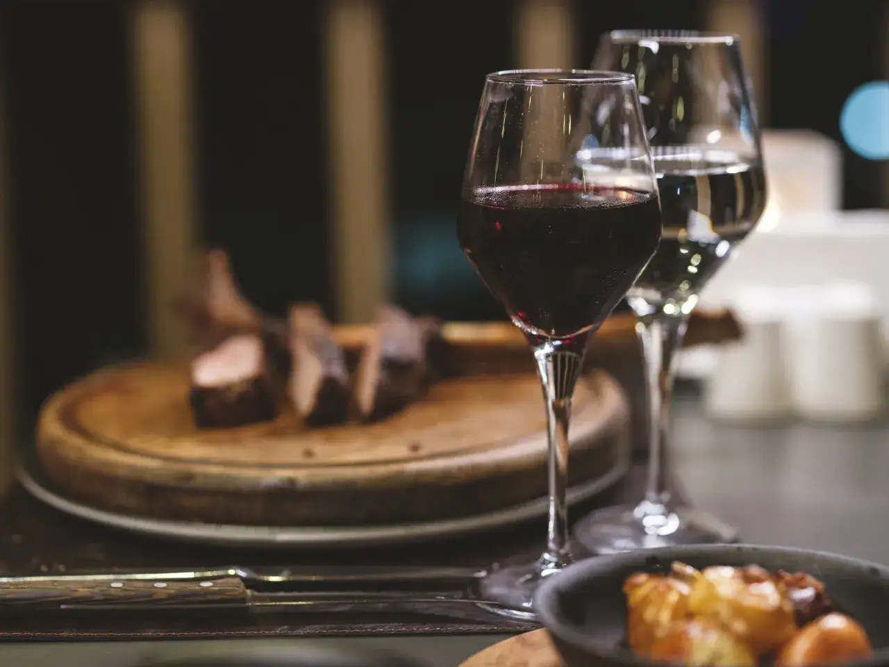 Verre de vin rouge, viande tranchée sur planche en bois, et un verre de vin blanc. Parfait pour accompagner un beaujolais nouveau.