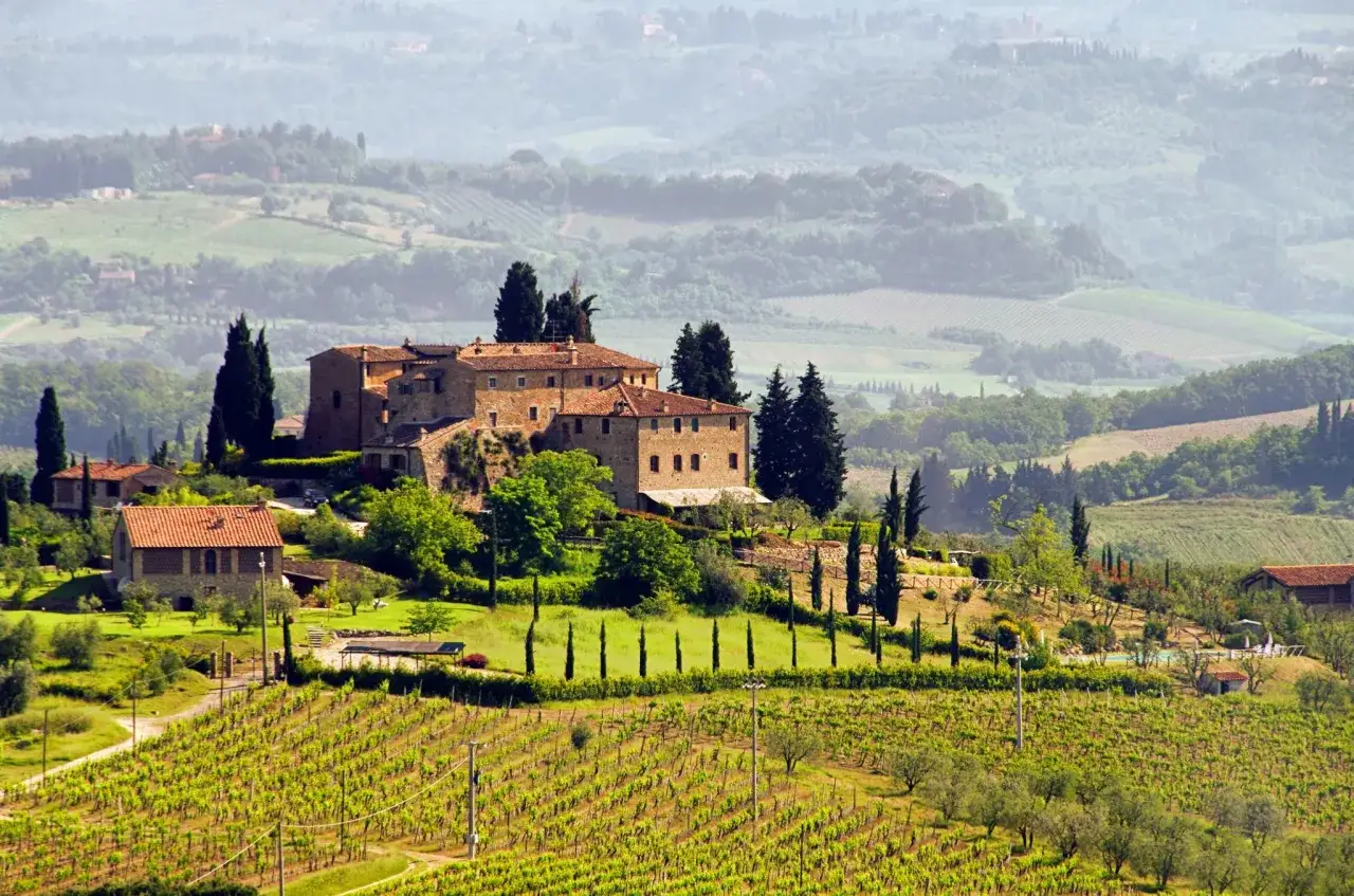 Collines toscanes verdoyantes, vignobles luxuriants et une ferme en pierre, évoquant les meilleurs vins italiens.
