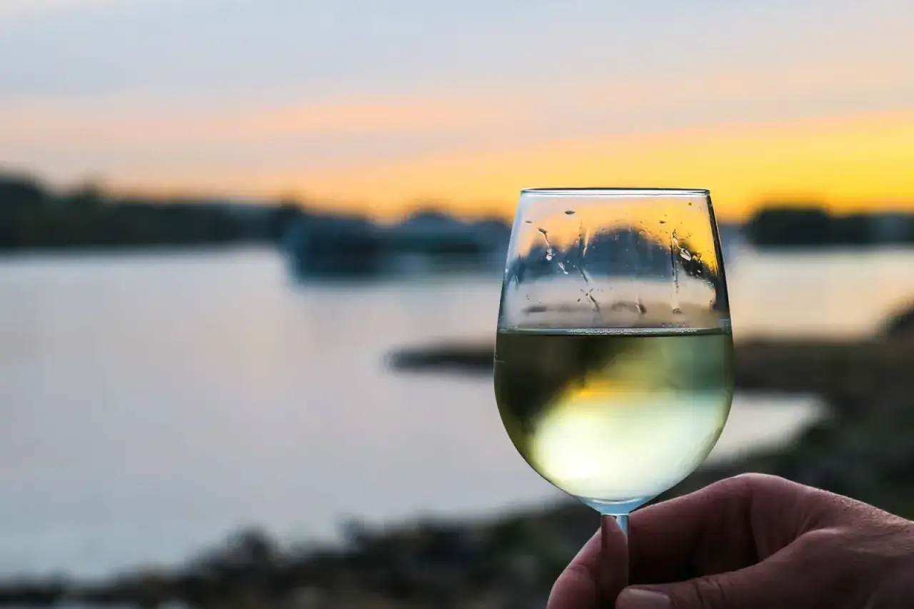 Un verre de vin blanc frais, parfait pour la conservation, tenu &agrave; la main au coucher du soleil sur l'eau.
