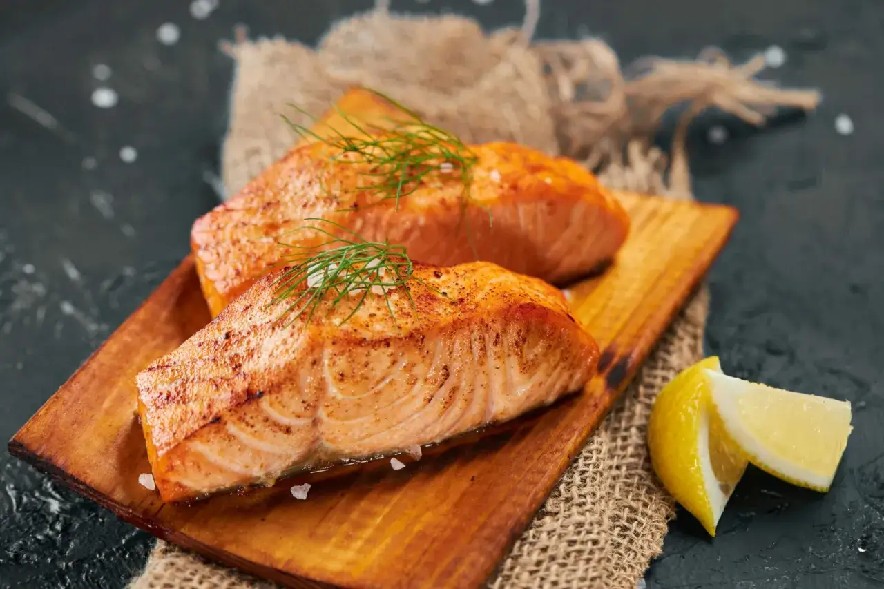 Deux pavés de saumon grillé, ornés d'aneth et de gros sel, sur une planche en bois. Parfait pour savoir quel vin avec du saumon.