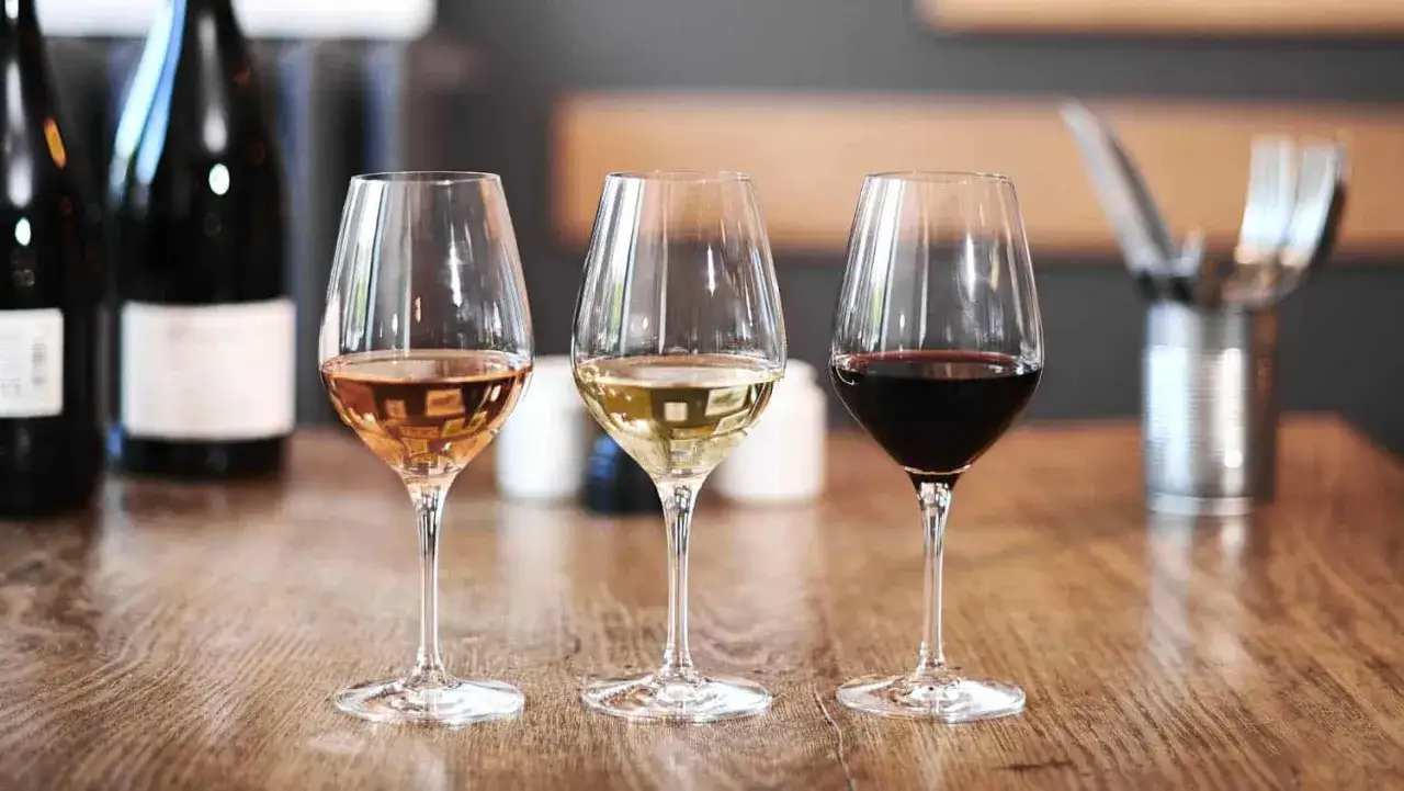 Trois verres de vin (rosé, blanc, rouge) sur une table en bois. Une invitation à tout savoir sur le vin.