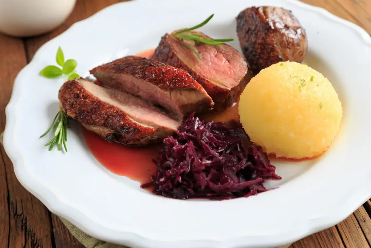 Magret de canard rosé, servi avec chou rouge et une quenelle de pomme de terre, le tout arrosé d'une sauce au vin. Un plat savoureux.
