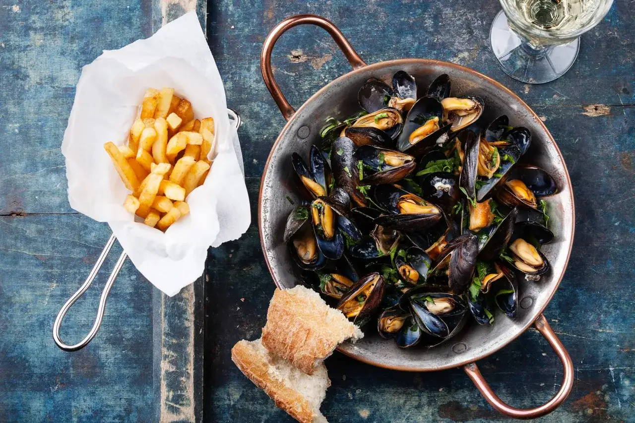 Un plat de moules marinières avec des frites croustillantes, du pain et un verre de vin blanc. Le parfait accord pour un