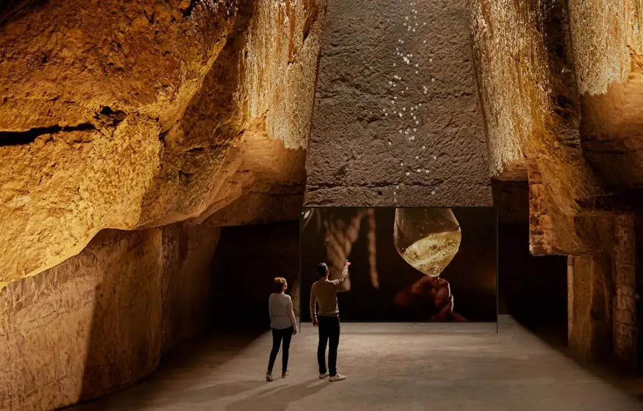 Deux visiteurs admirent une projection d'un verre de vin pétillant dans les caves Ackerman à Saumur, un prix d'excellence pour ce lieu historique.