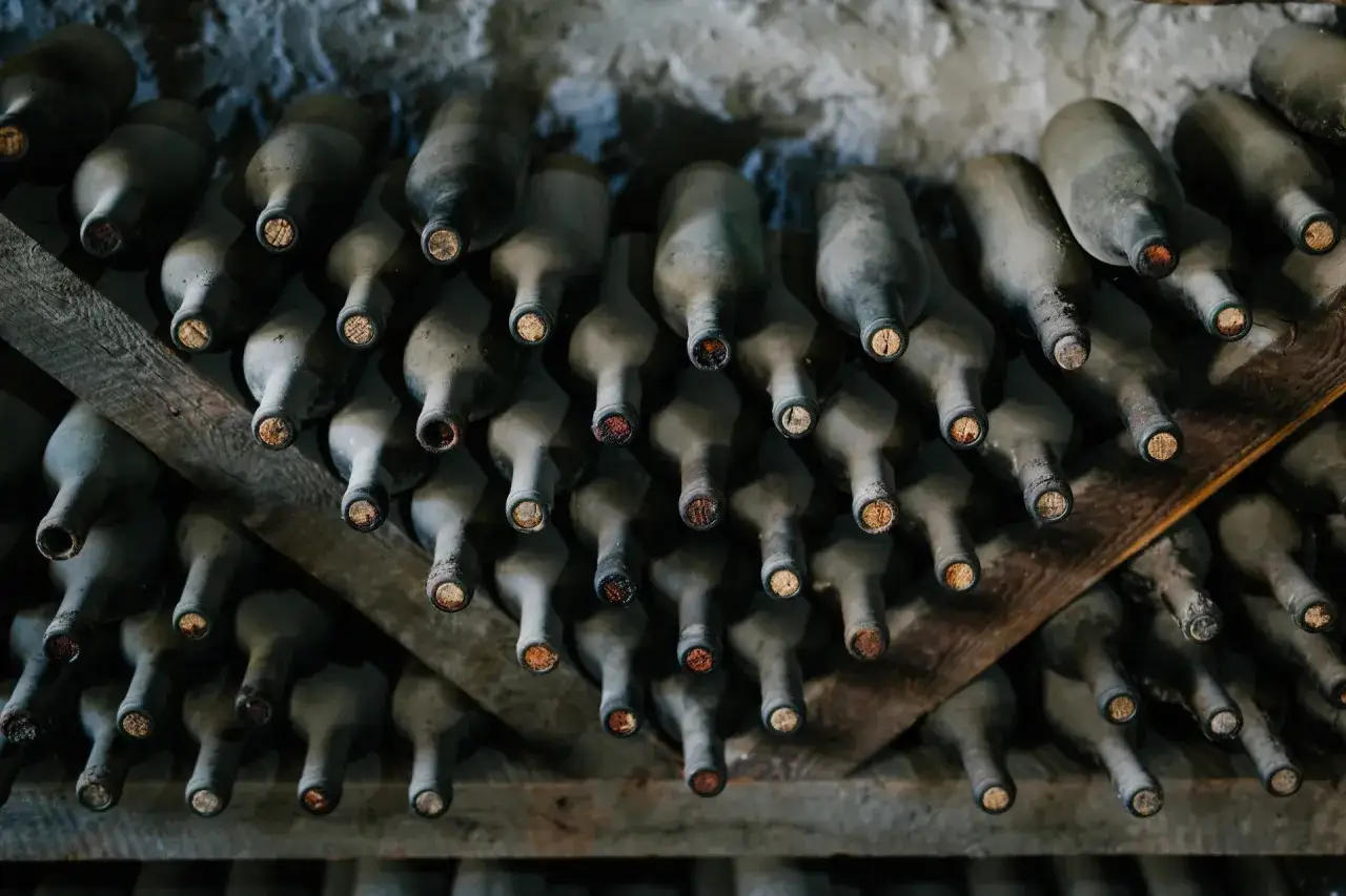 Des bouteilles de vin anciennes, poussi&eacute;reuses, stock&eacute;es sur des &eacute;tag&egrave;res en bois. Id&eacute;al pour apprendre comment r&eacute;gler une cave &agrave; vin &eacute;lectrique.